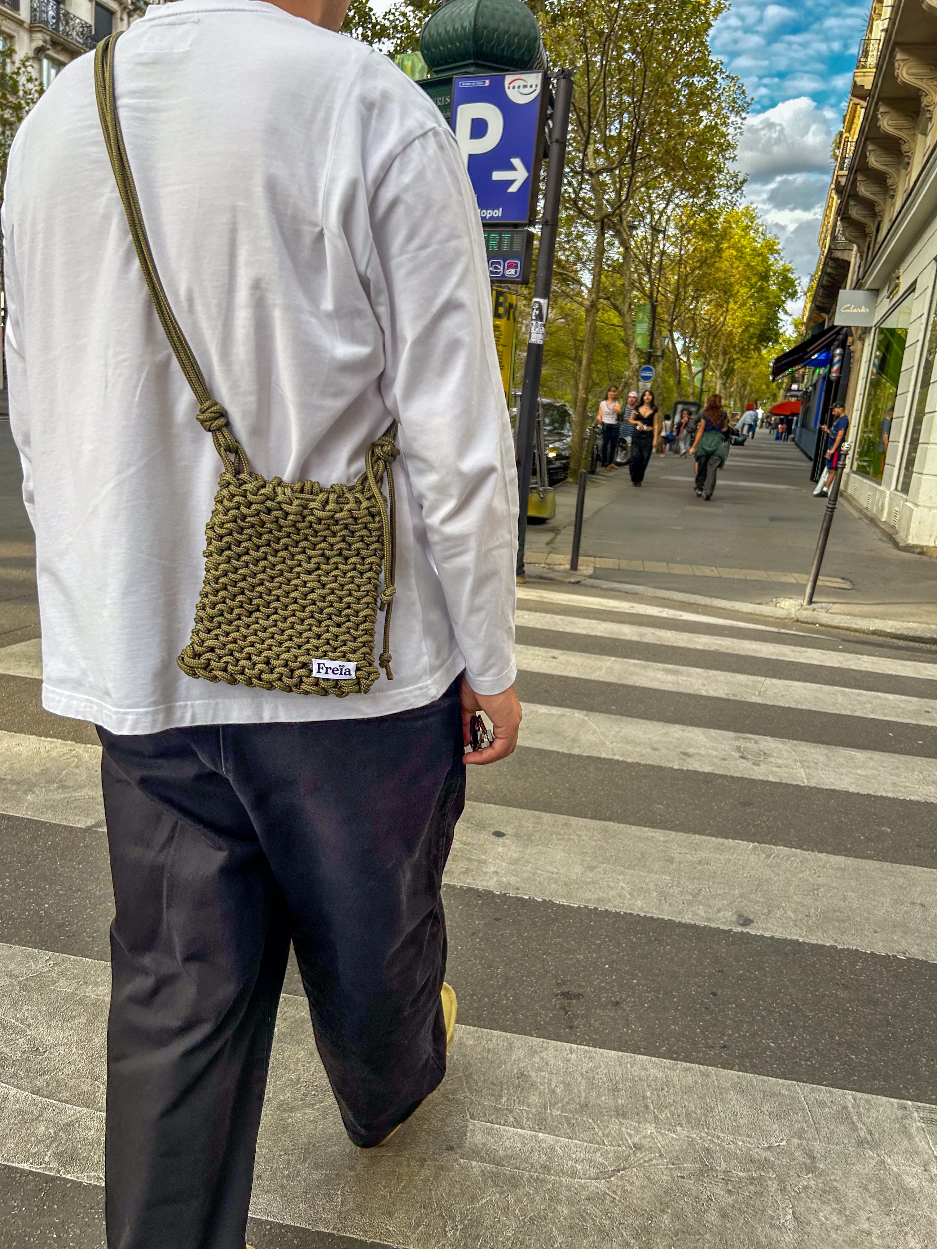 Homme de dos avec un sac Freïa en paracorde kaki sur un passage piéton parisien